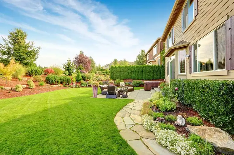 Finished landscaped backyard with a striped green lawn, stone pathway, patio and planted beds