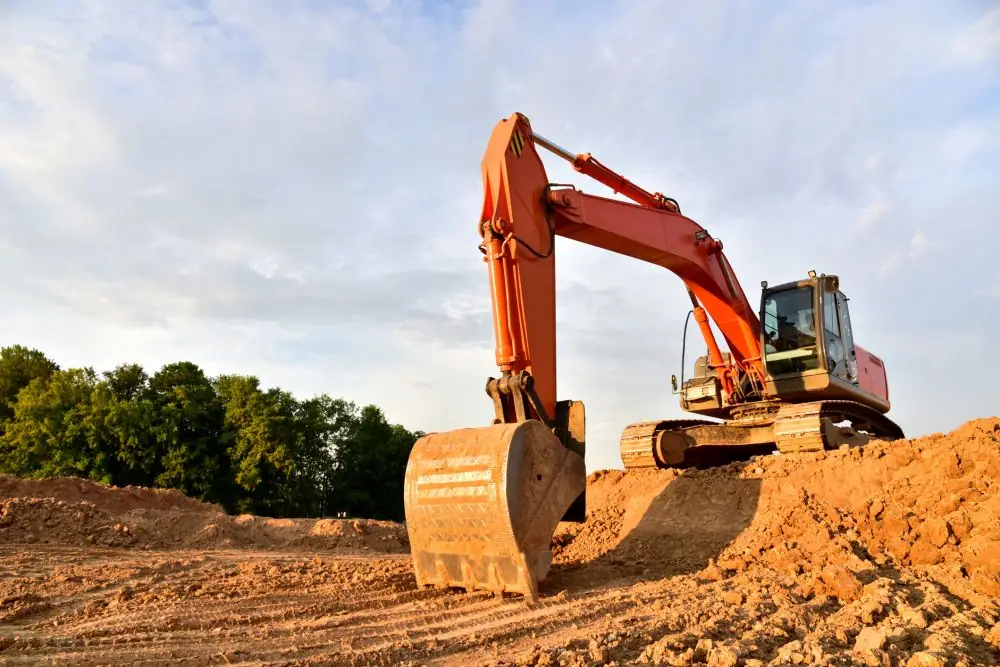 Orange excavator grading and levelling bare earth on a work site
